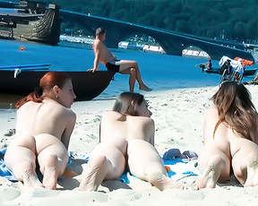 Three Nudists Resting on Blue Towels Near Moored Boats