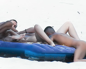 Tři nudisté sdílející modrou nafukovací matraci na písku
