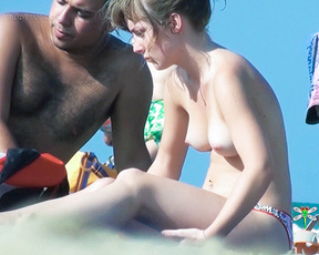 Two Adults Resting on Sand at a Topless Beach
