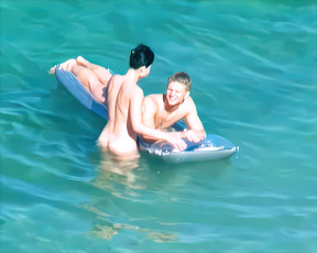 Two nudists lounging together on a blue raft in sunlit turquoise water