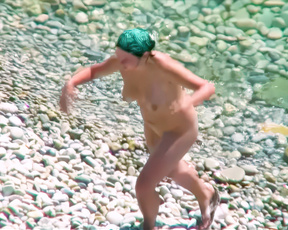 Nudist woman splashing through sunlit pebbles in shallow clear water