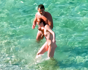 Two nudists hold close in bright turquoise open shallows