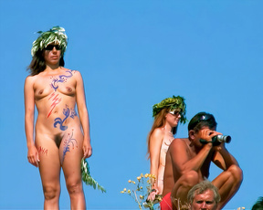 Body-painted nudists posing outdoors beneath a bright blue sky