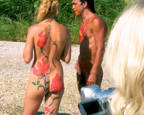 Nudists in vivid body paint facing each other on a sunlit path