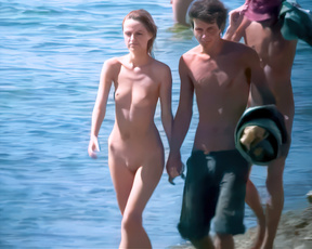 Nudist woman wading through sunlit water beside a man at the shoreline