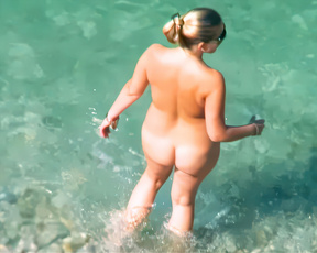 Blonde nudist woman wading through sunlit turquoise shallows