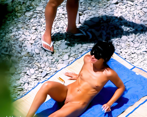 Nudist woman sunbathing on pebbles beside a striped beach towel