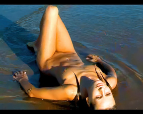 Nudist woman reclining in shallow sunlit shoreline water