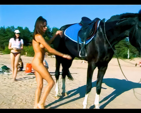 Naturistka stojí nahá vedle osedlaného černého koně