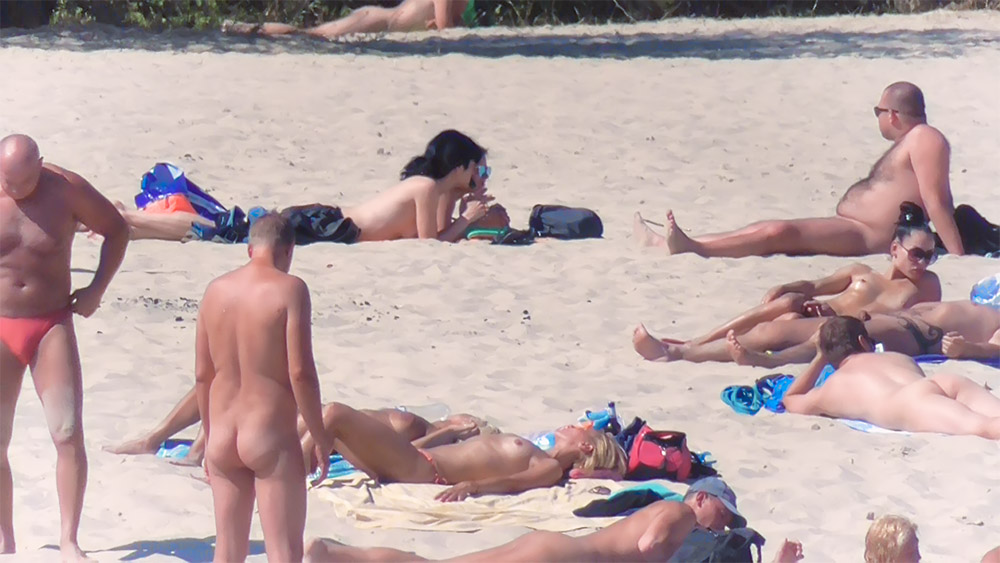 Four Nudists Sunbathing Close Together on Bright Sand