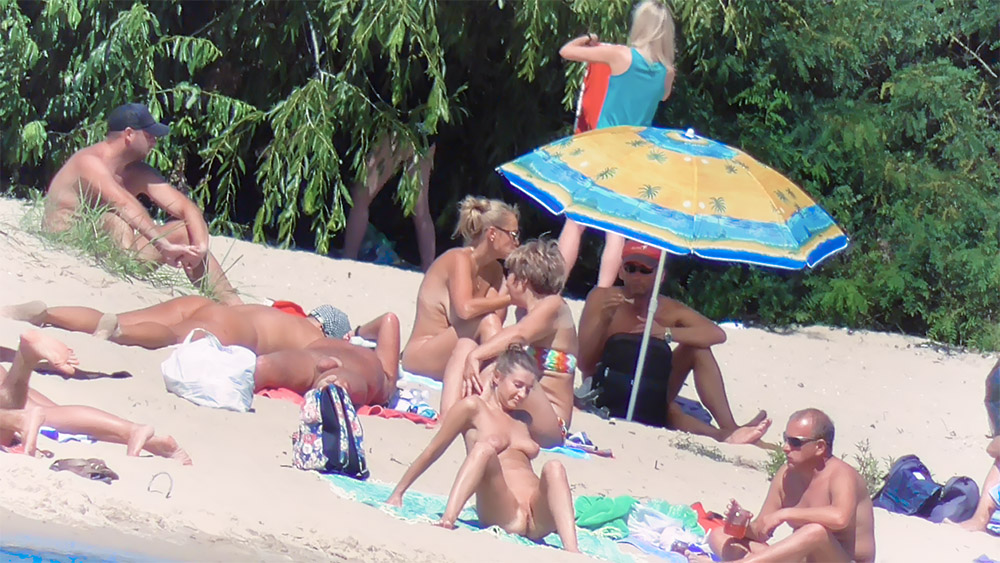Odpoledne na písečné nudistické pláži pod pruhovaným slunečníkem