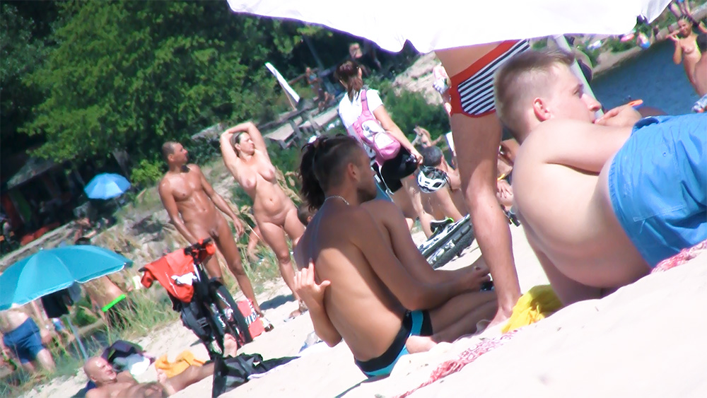 Six Naturists Standing and Sitting on a Busy Beach