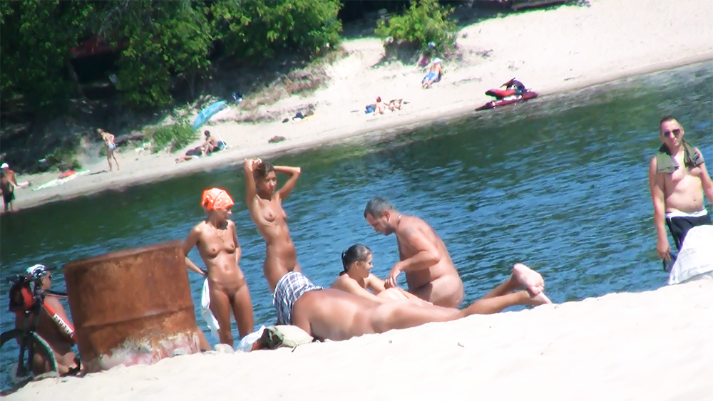 Four Nudists Standing and Sitting by a Small River
