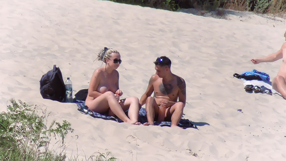 Sandy Nudist Beach Couple with a Sunscreen Bottle