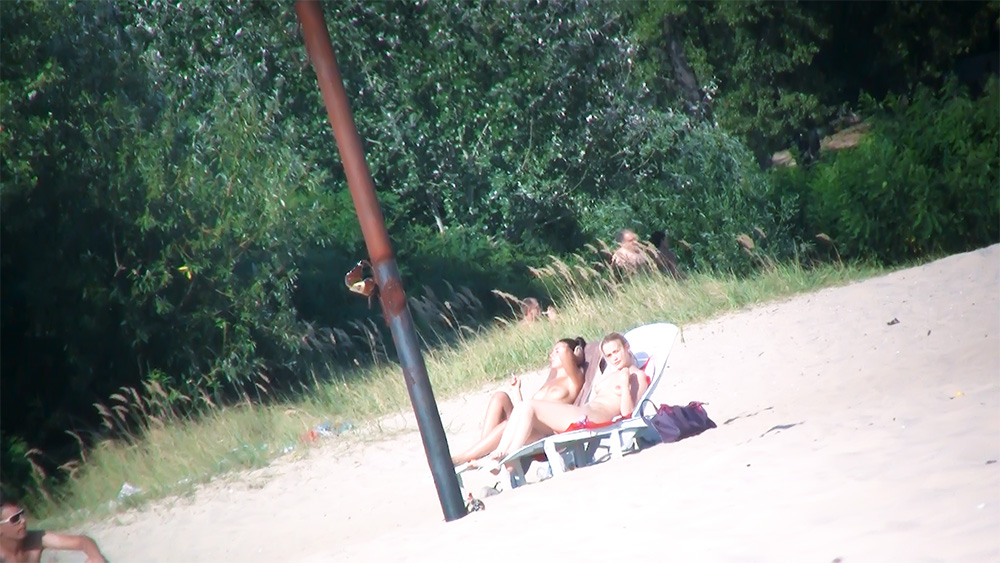 Two Women Topless on Beach Loungers Near Tall Grass