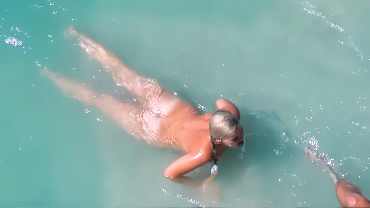 Nudist woman floating relaxed in sunlit turquoise shallows
