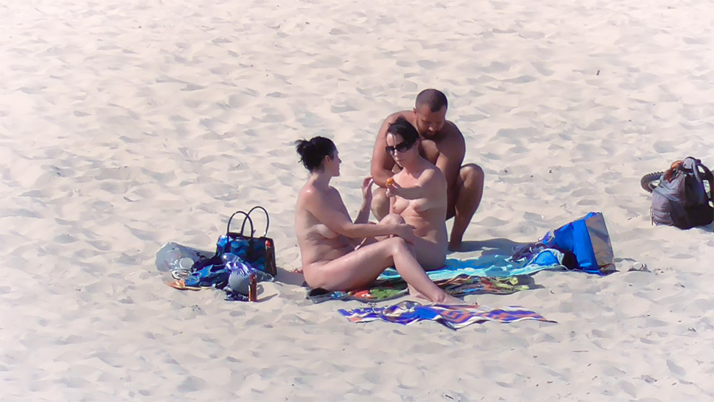 Tři nudisté sdílejí vzorovaný ručník na písku