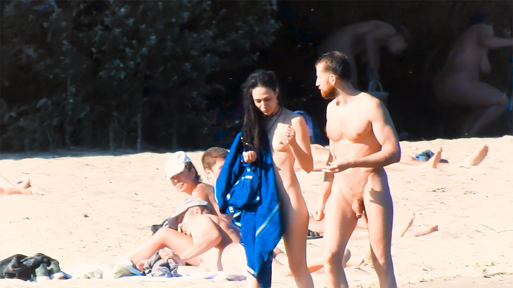 Two Nudists Conversing on the Sand with Blue Bundle