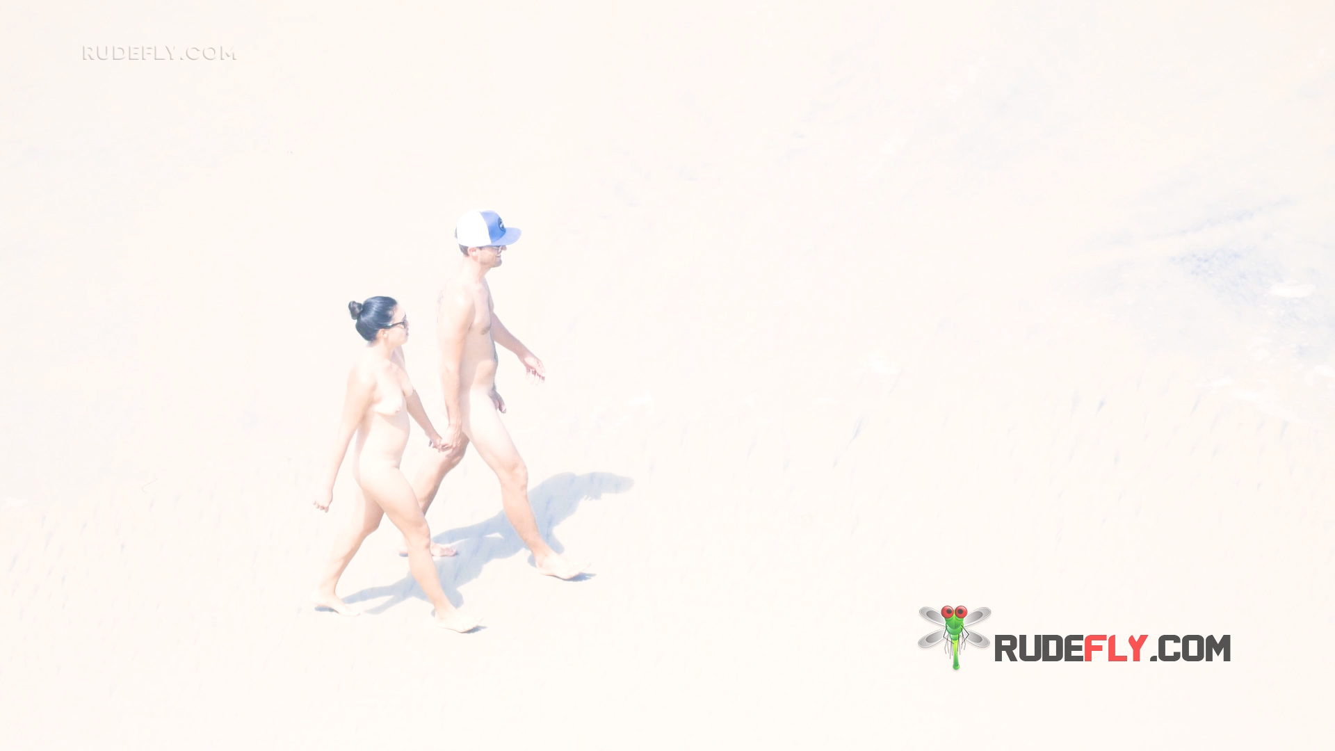 Zwei Naturisten richten sich unter einem gestreiften Strandschirm ein