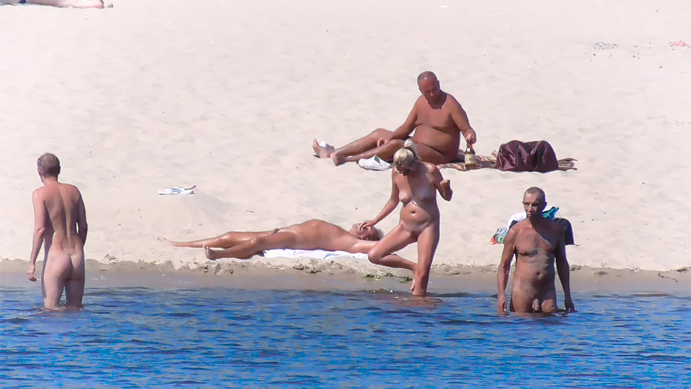 Four Naturists Resting Near the Water on a Sandy Beach