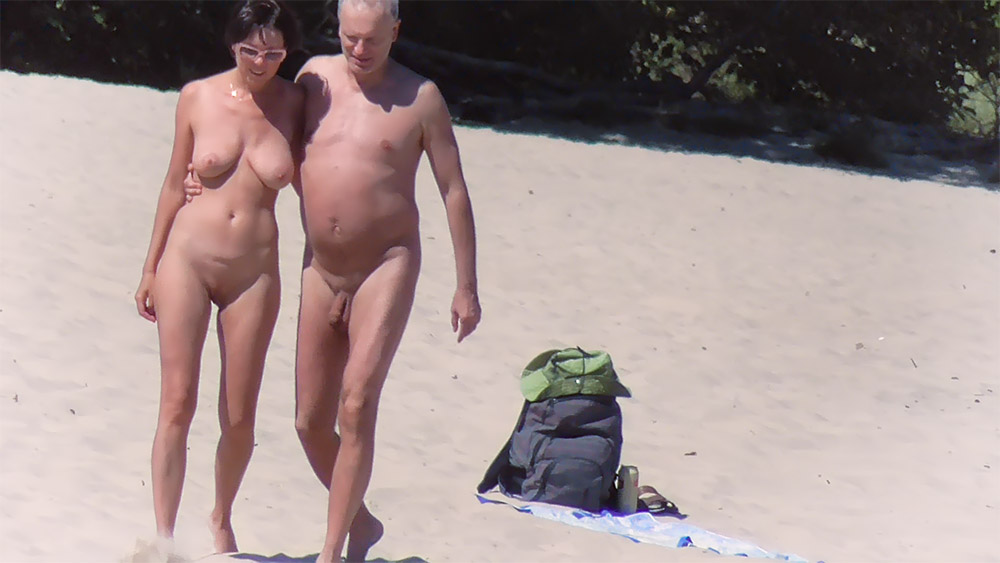 Písečná nudistická pláž s jasně zeleným batohem