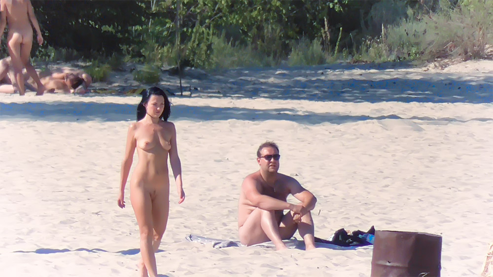 Ciemnowłosa kobieta i siedzący mężczyzna na plaży dla naturystów