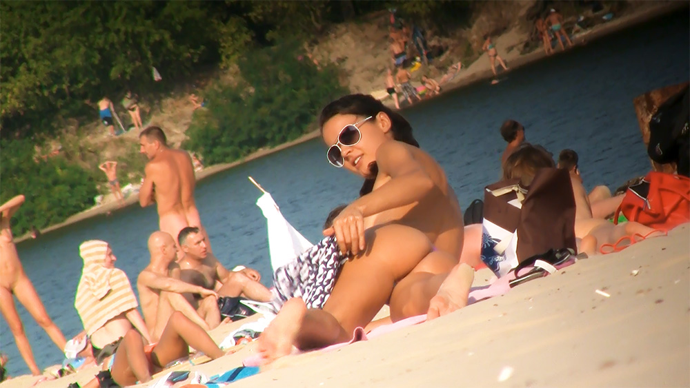 Occhiali da sole tondi e pareo a motivi su una spiaggia naturista