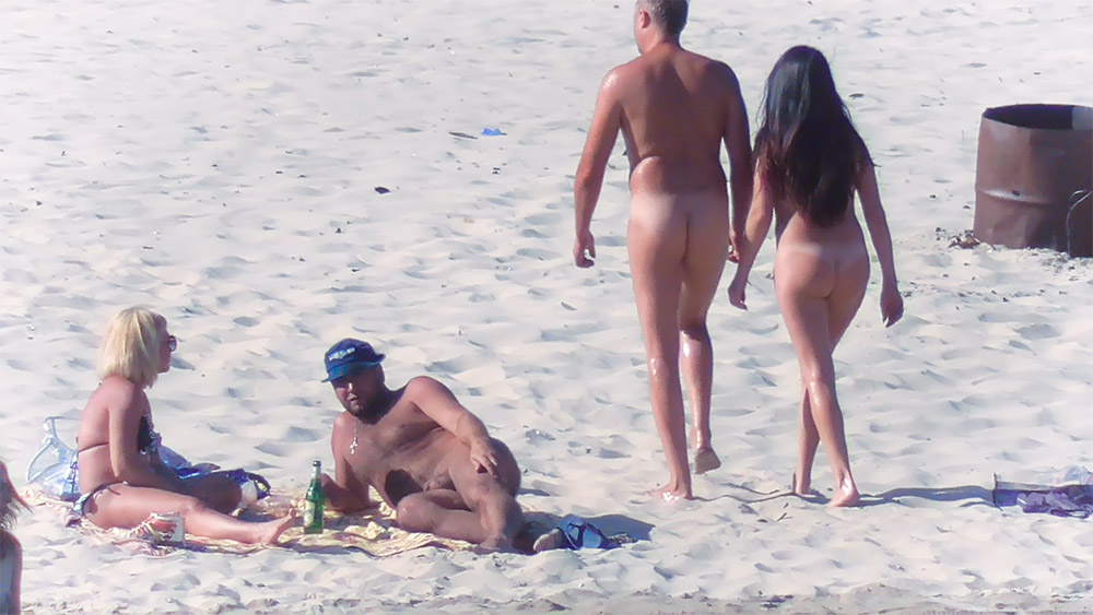 Nude Beach Couple Passing a Metal Barrel on Sand