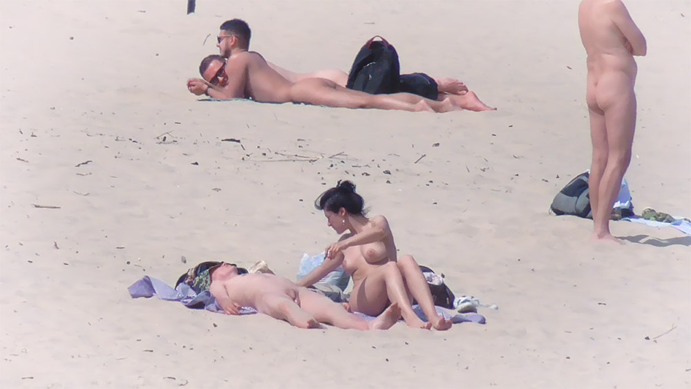 Vijf nudisten rustend op handdoeken over het zand