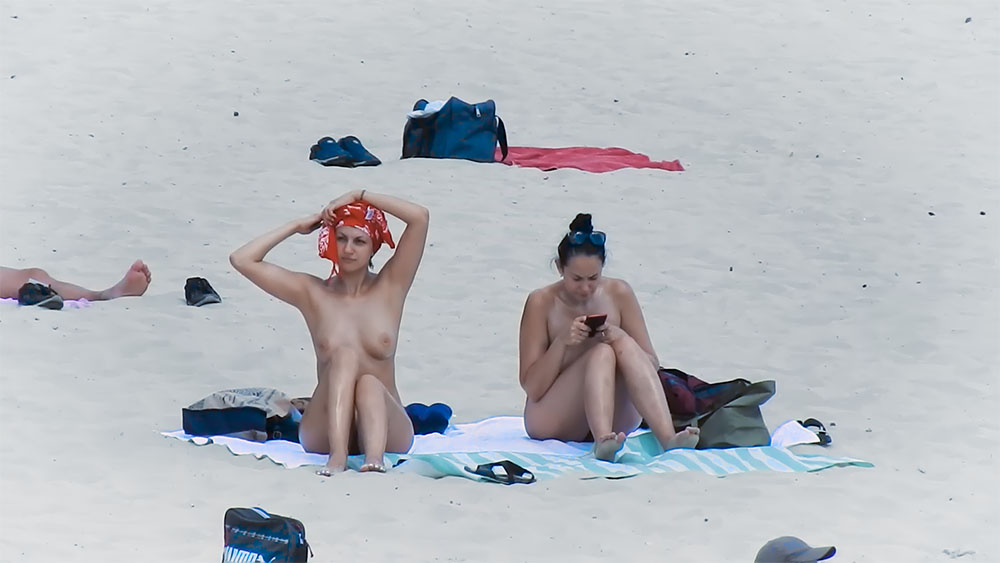 Duas Mulheres numa Praia Nudista com Lenço Vermelho e Telemóvel