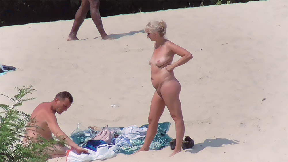 Mulher Loira Entre Nudistas ao Lado de uma Toalha com Padrões