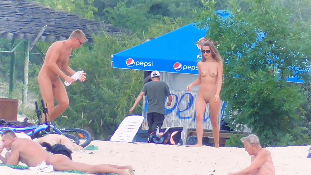 One Nudist Posing on Sand Near a Pepsi Umbrella