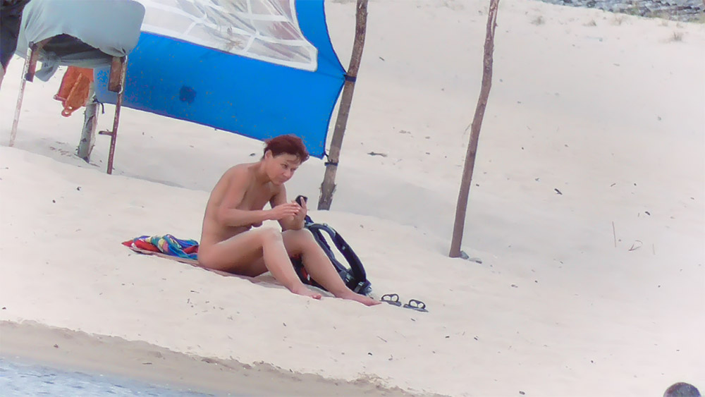 Checking Phone on a Nude Beach Towel Under Blue Shade