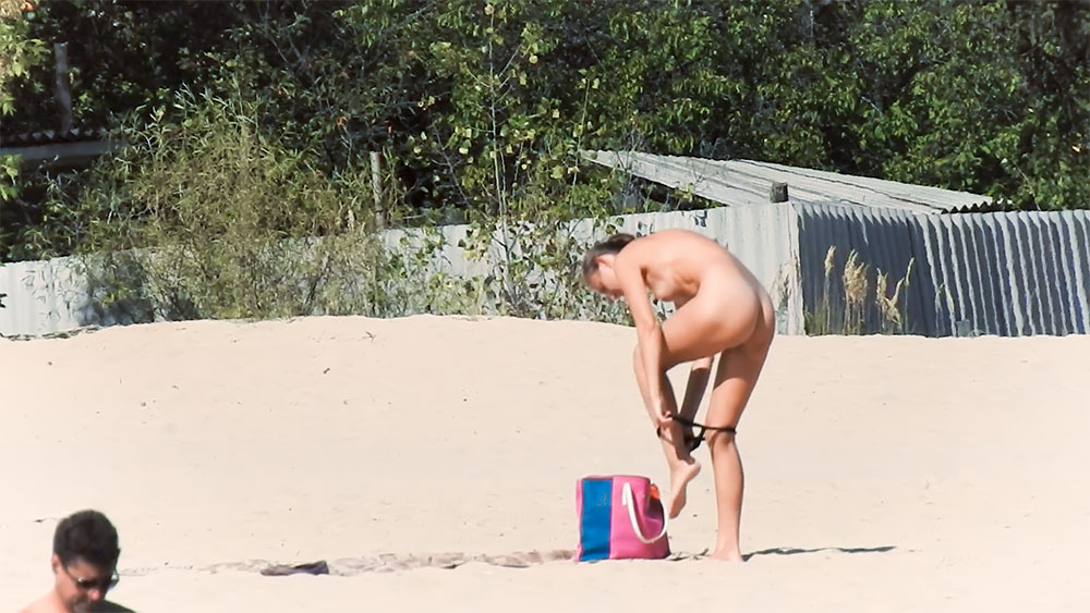Nudistka se obléká vedle růžové plážové tašky