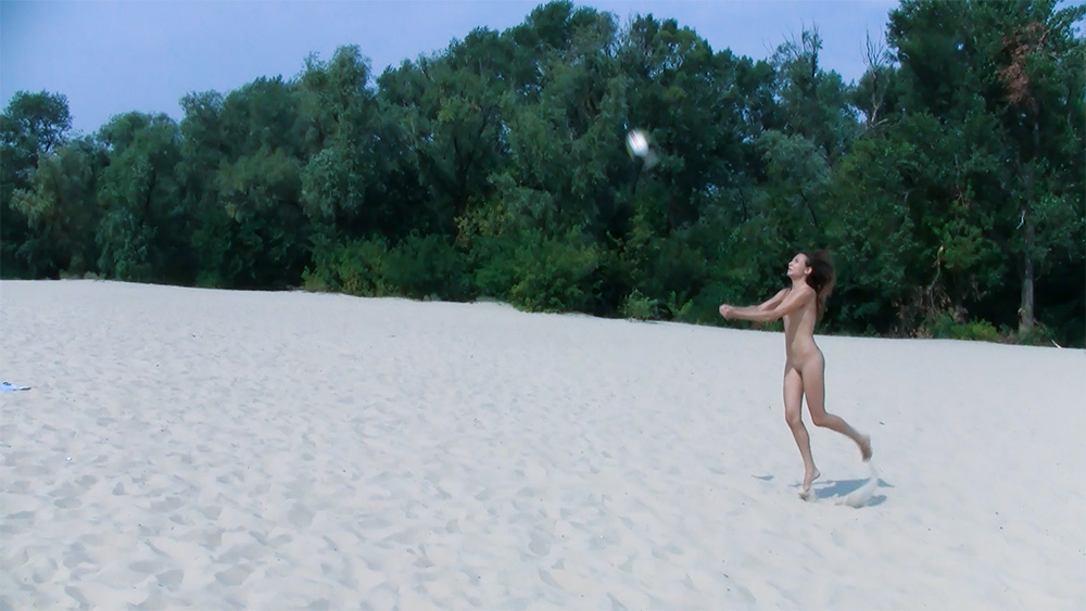Zwei Nudisten werfen sich einen Volleyball am sandigen Flussufer zu