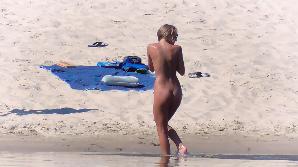 Nudistka míří k vodě přes teplý písek