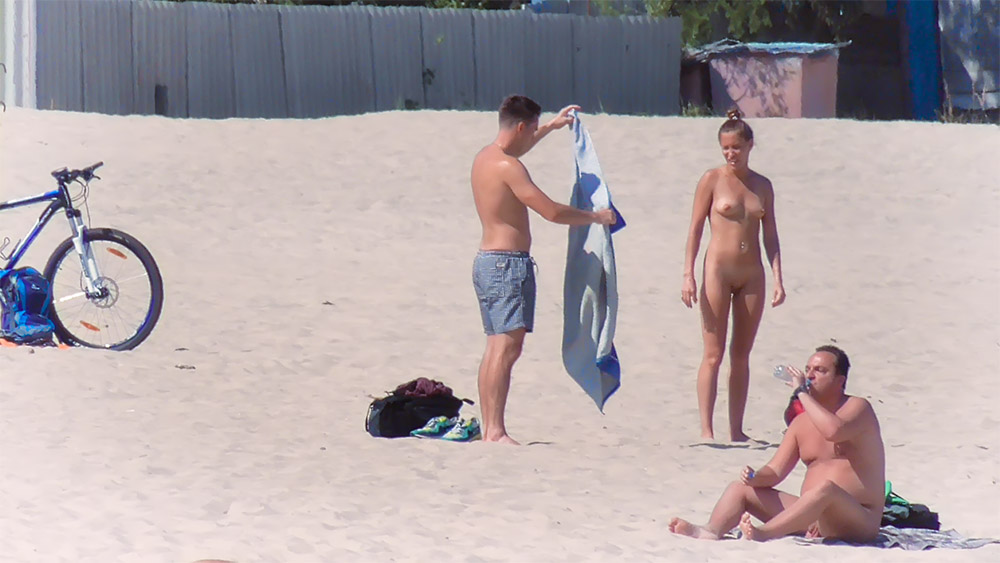 Three Nudists Settling In on a Sandy Beach