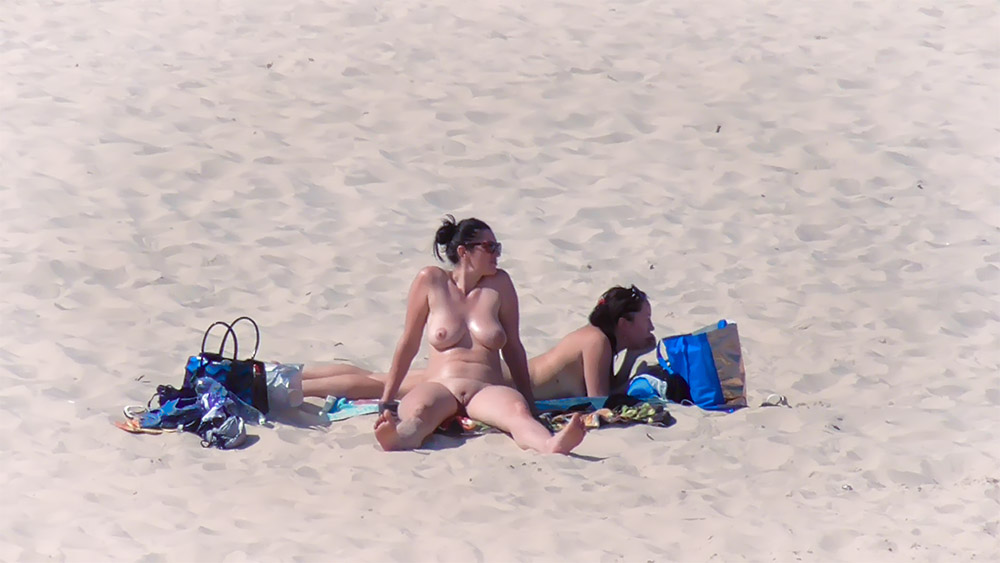Two Nudists Sitting on a Bright Sandy Beach
