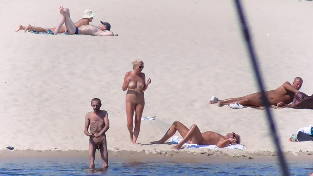 Two Nudists on the Sand Near Calm Water