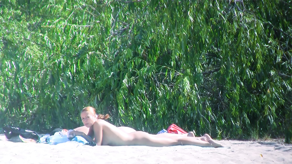 Tumbada boca abajo sobre una toalla en una tranquila playa nudista