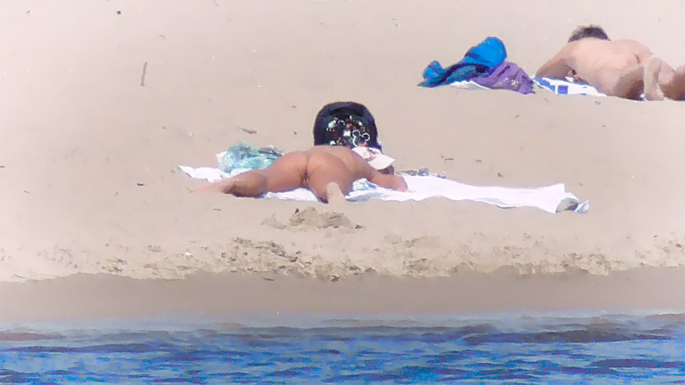 Toalla de playa nudista y cojín oscuro sobre arena pálida