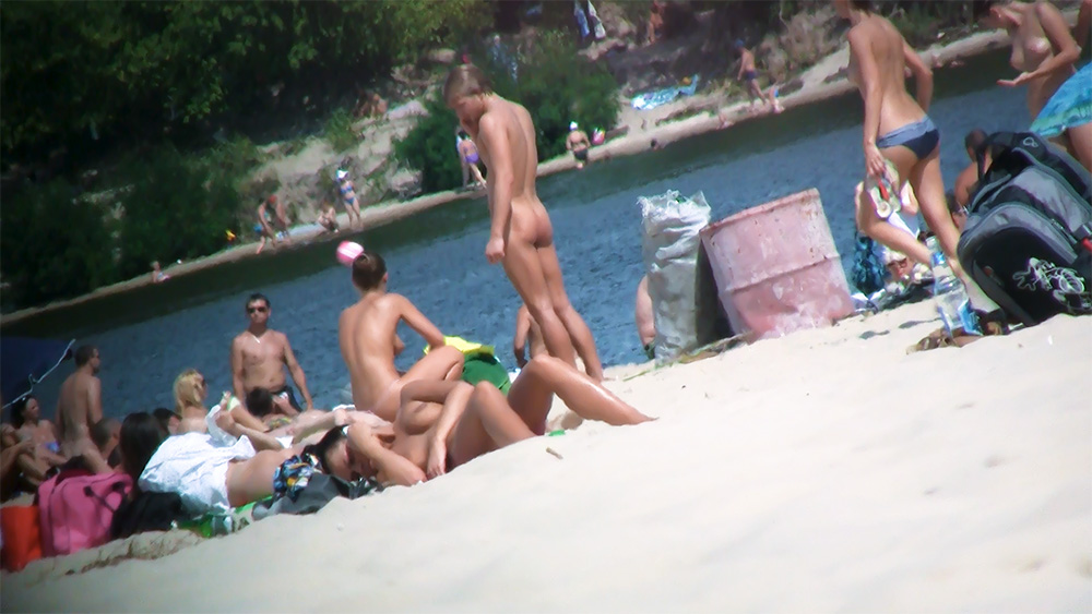 Four Nudists Resting Together on Bright Beach Sand