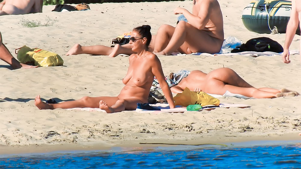 Opalující se dívka ve slunečních brýlích s vlasy v drdolu na nudistické pláži