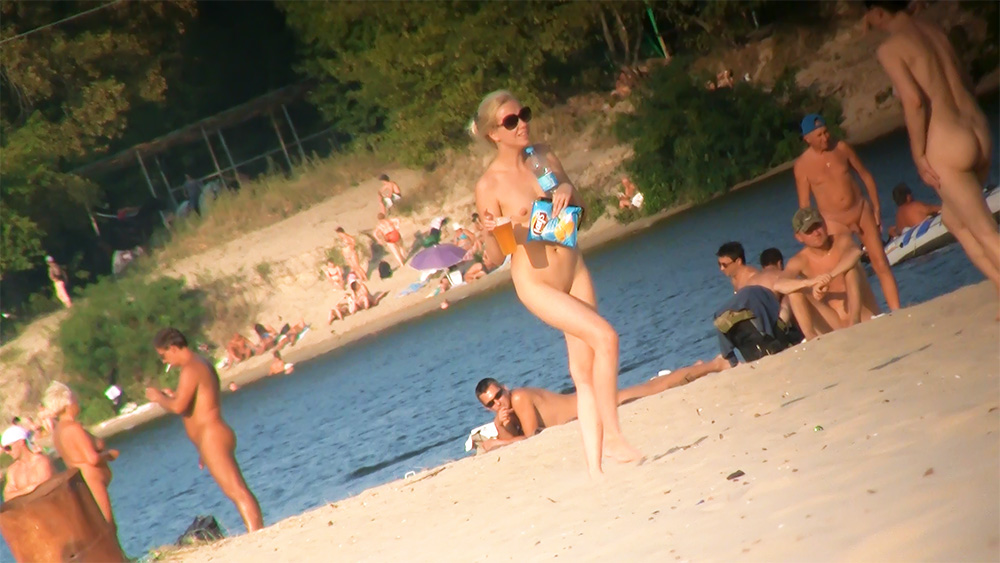 Nudistická pláž u řeky s blondýnou držící svačinu