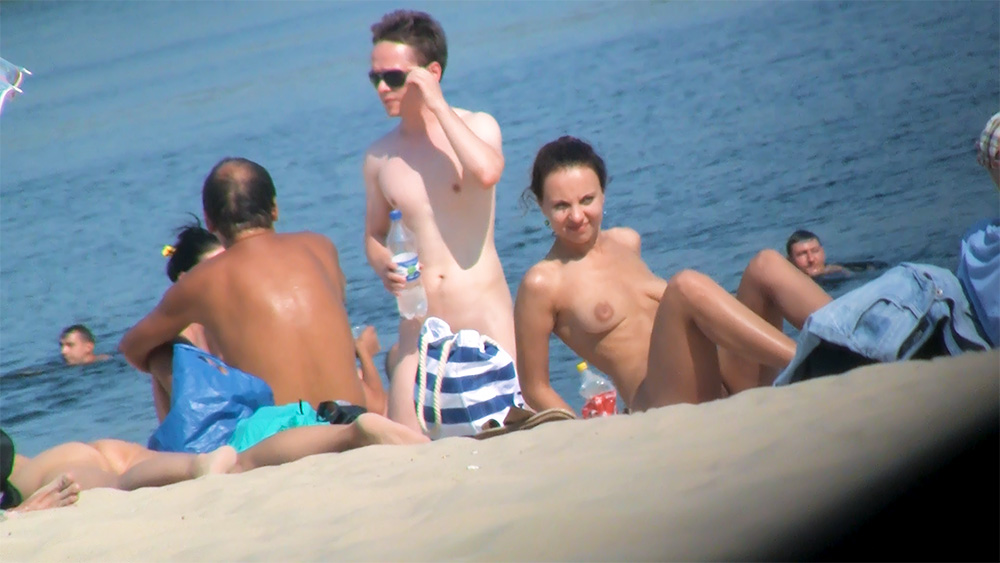 Torba w paski na piasku obok opalających się na plaży nudystów