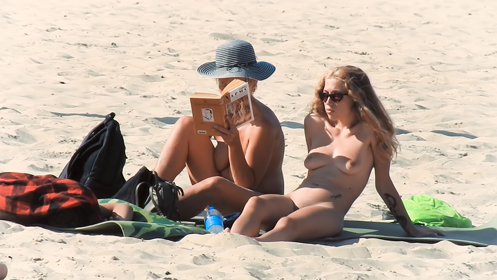 Two Nudists Sitting on a Sandy Beach with Sun Hat