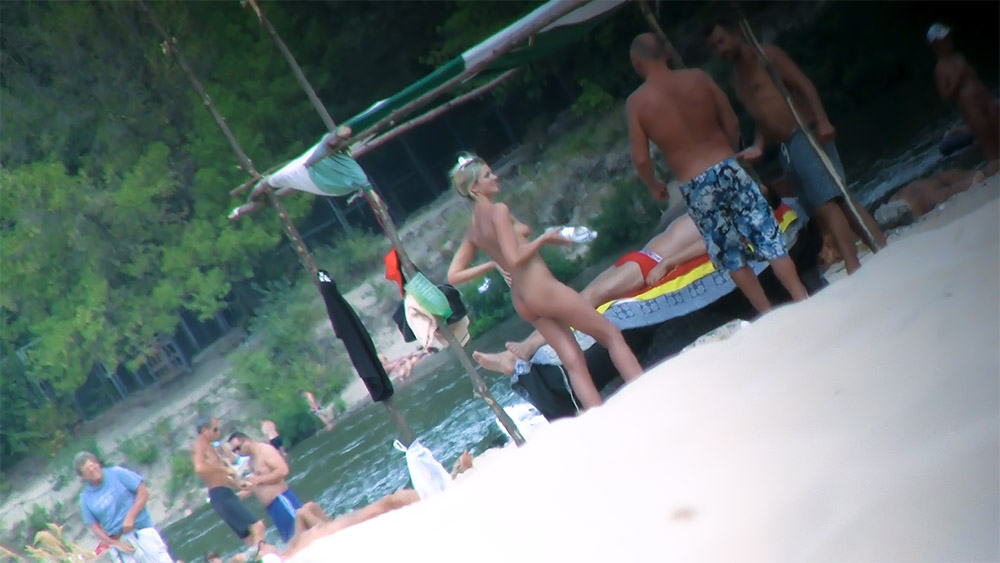 Naturists Standing Near a Colorful Raft by the Water