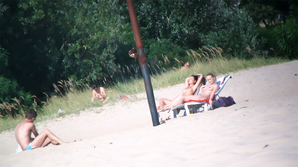 Two Nudists Sunbathing Side by Side on Beach Chairs