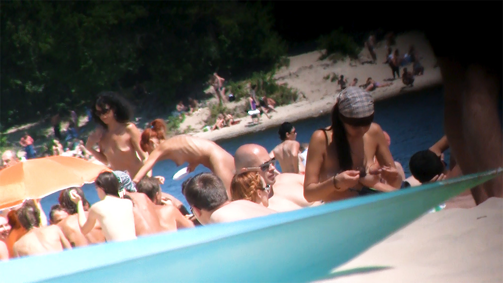 Wading Through Shallow Water at a Crowded Nudist Beach