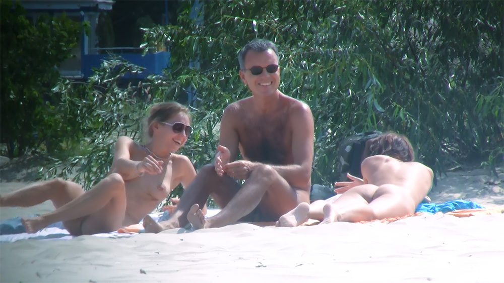 Sezení a gestikulace na stinné nudistické pláži